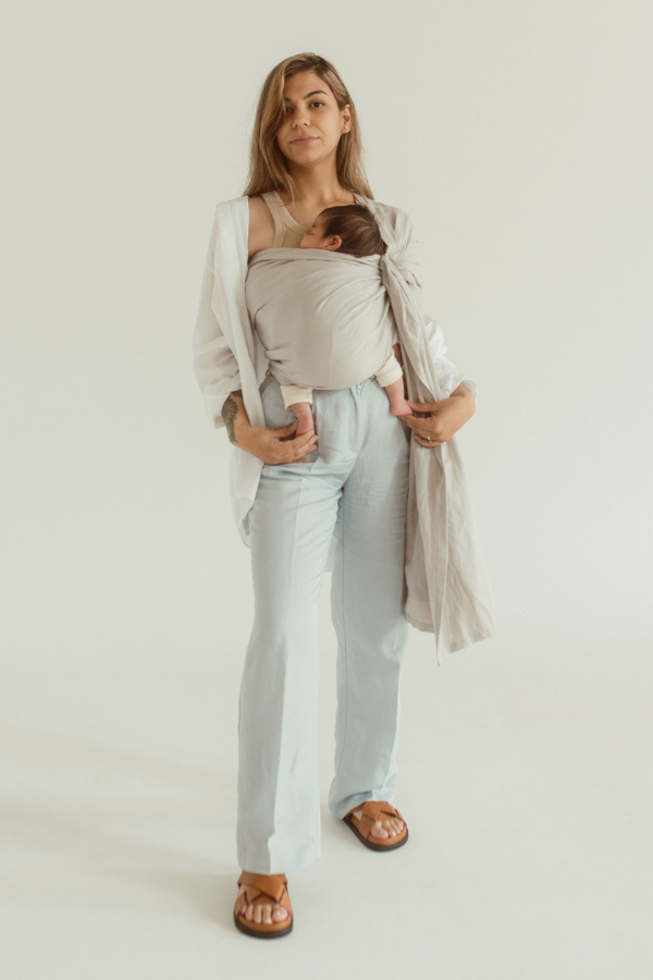 A mother wears her newborn baby close in a Ring Sling Carrier, in the shade Asha - a neutral soft grey tone.