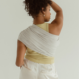 A mother holds her hair up to show off the  back of the Ring Sling designed by Chekoh. It is made of linen and bamboo in a grey and white woven print.