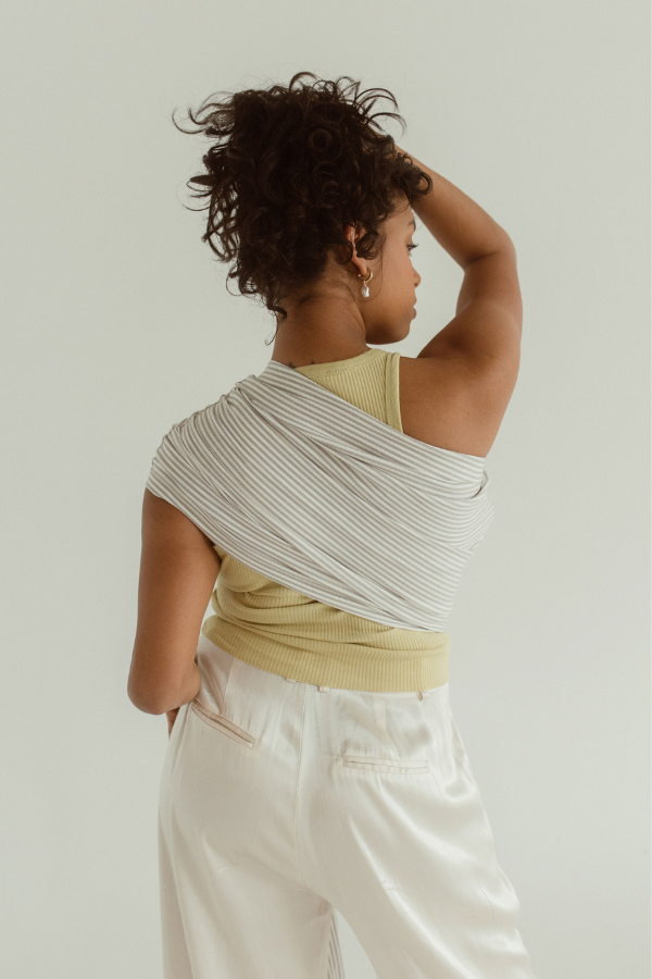 A mother holds her hair up to show off the  back of the Ring Sling designed by Chekoh. It is made of linen and bamboo in a grey and white woven print.