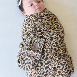 Newborn baby with fluffy hair is swaddled up in the animal Leopard Print design featured on the Chekoh Baby Leopard Swaddle Wrap. Baby looks calm and content.